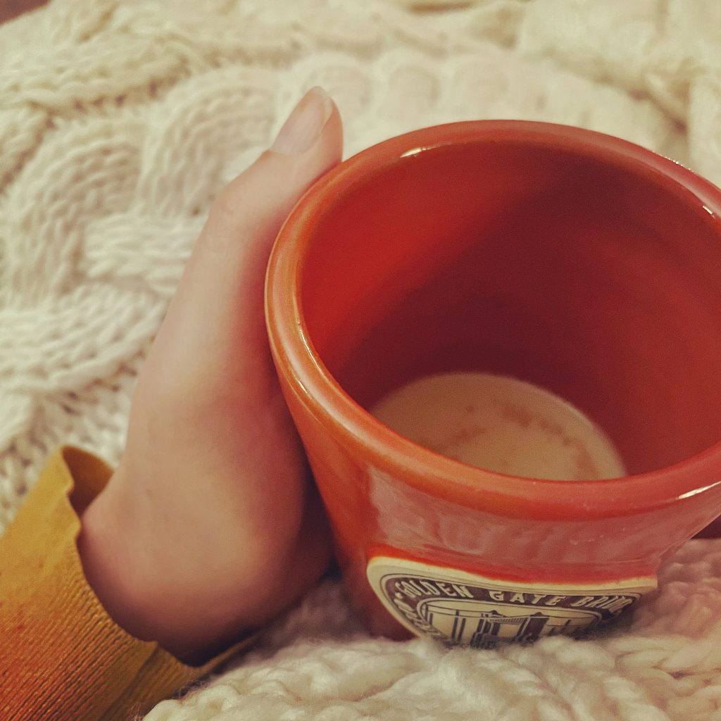 Girl wrapping hand around hot coffee in a cozy blanket. Press on Weary Momma